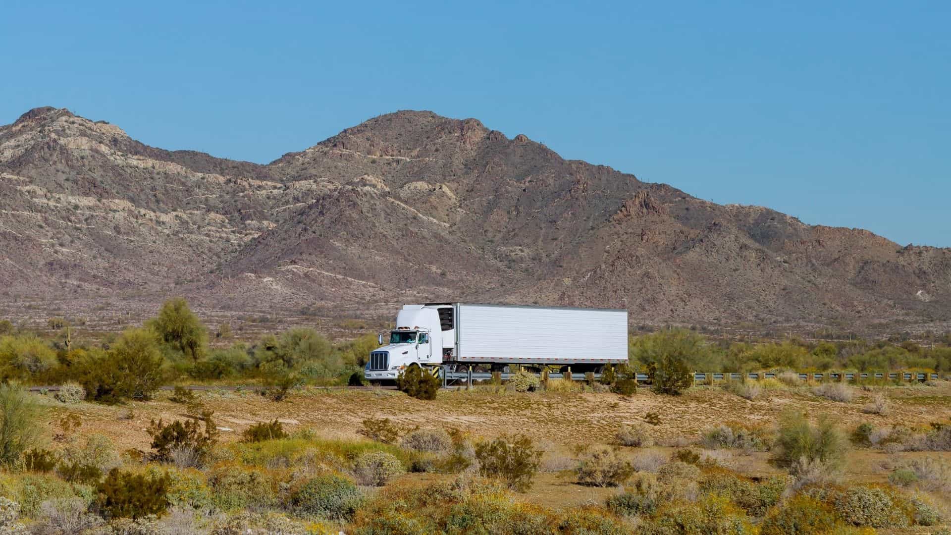 Refrigerated truck transporting temperature-controlled goods through a hot desert landscape, illustrating cold-chain logistics under high-heat conditions.