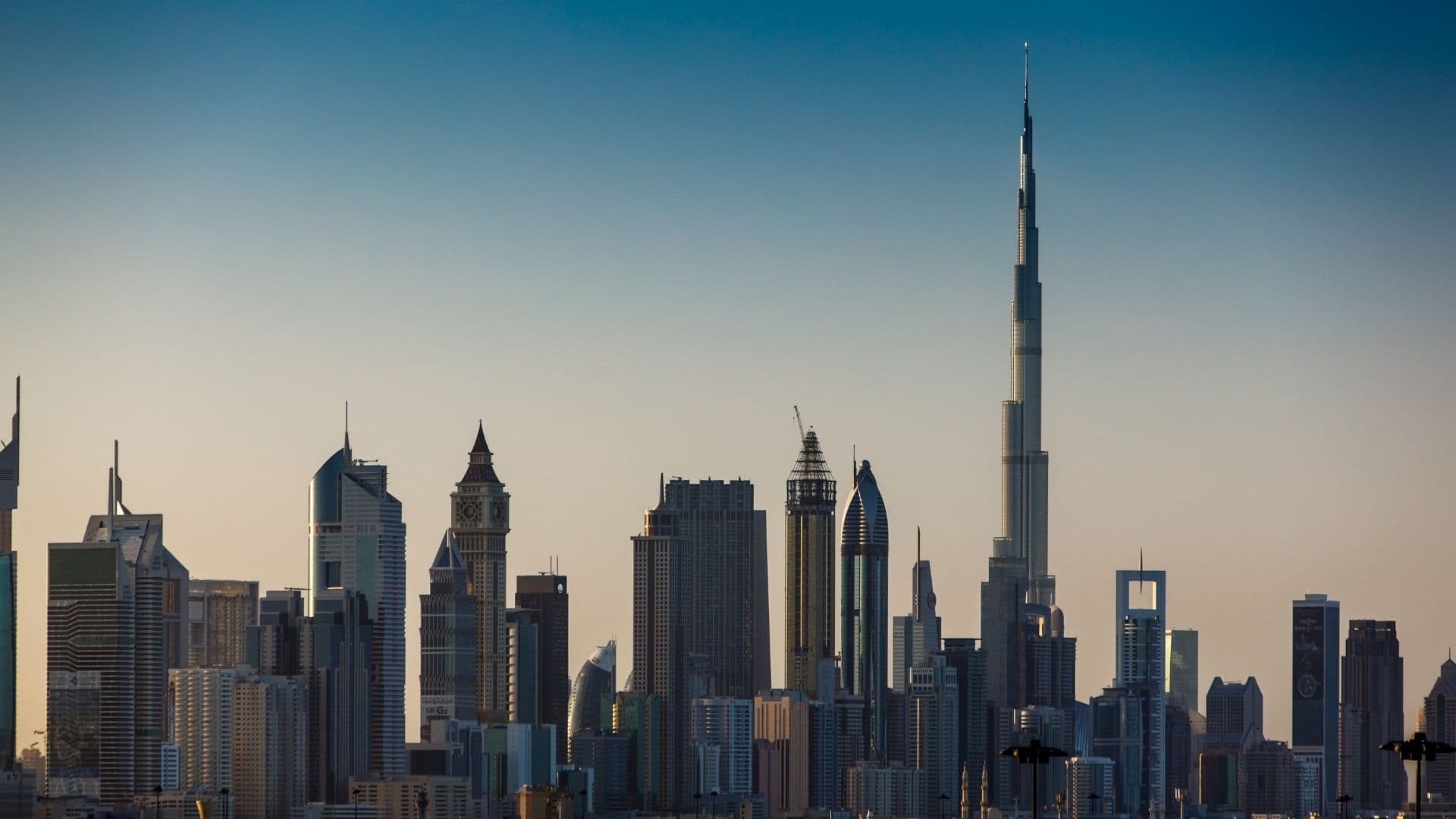Dubai skyline at dawn, with the Burj Khalifa rising above dense high-rise towers under a clear sky.
