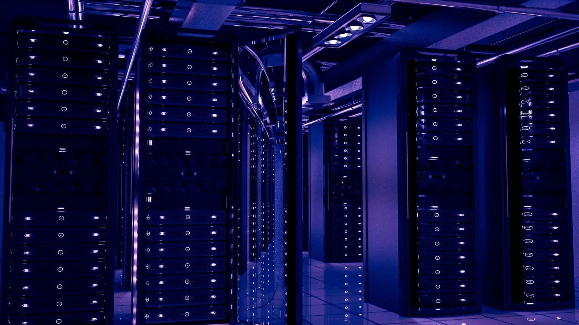 Rows of server racks under purple lighting with overhead cooling ducts in a data centre hall.
